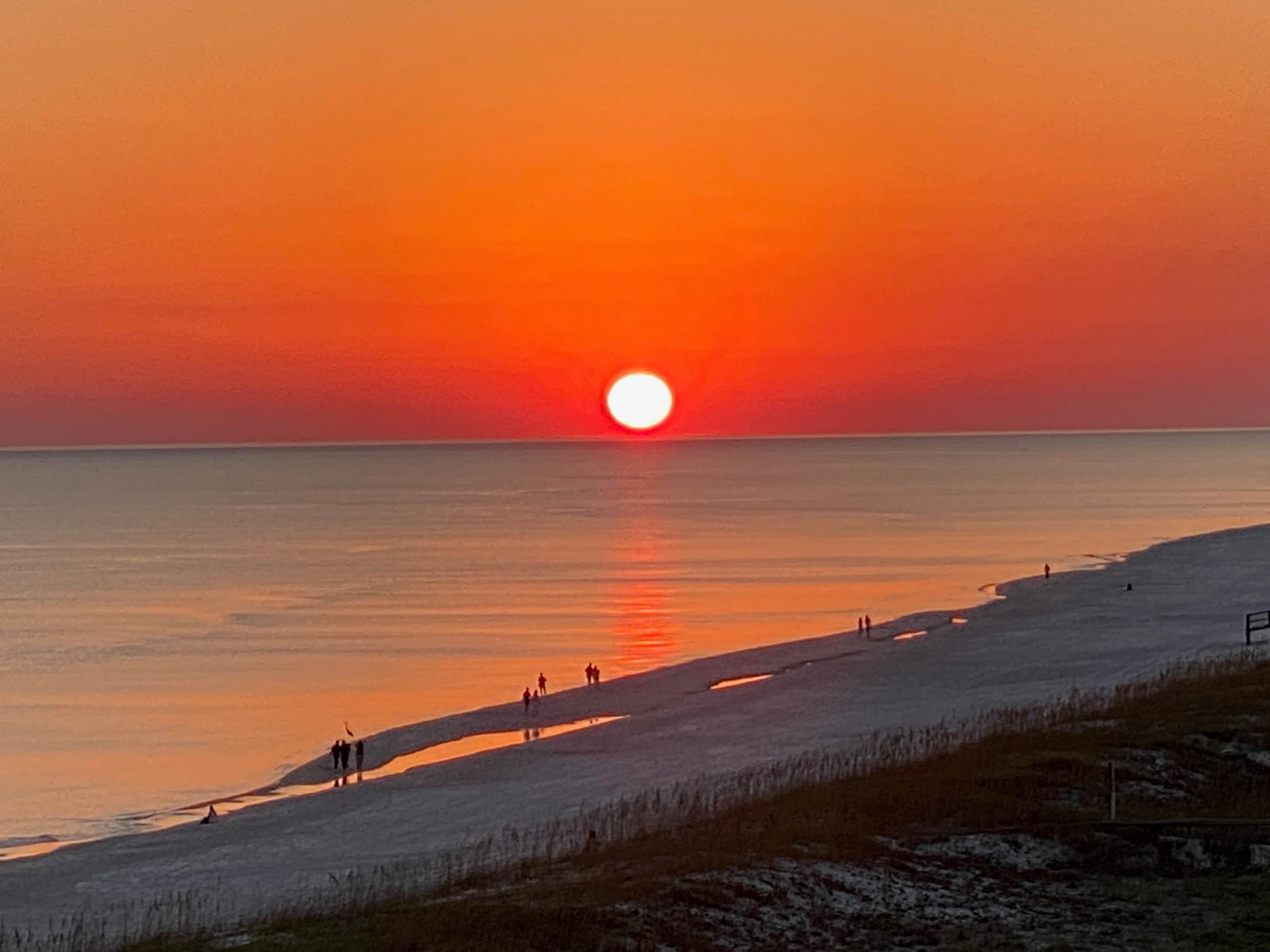 A sunset over a beach with people walking along the shore.