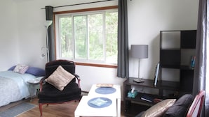 Uma sala de estar aconchegante com uma cama, uma poltrona, uma mesa e uma estante de livros.