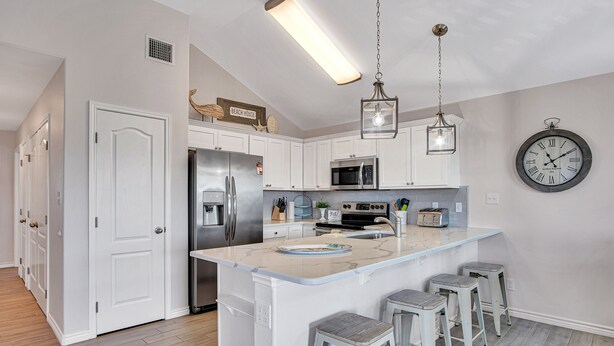 A modern kitchen with white cabinets, stainless steel appliances, a large island with bar stools, and a wall clock.