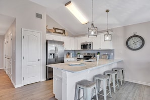 A modern kitchen with white cabinets, stainless steel appliances, a large island with bar stools, and a wall clock.