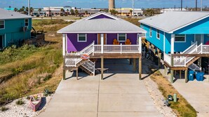 A beachfront house with a wooden deck, a small porch, and a view of the ocean.
