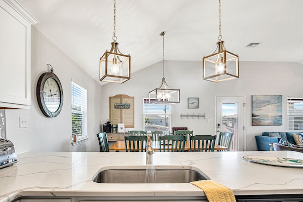 A kitchen with a marble countertop, a sink, and hanging pendant lights.