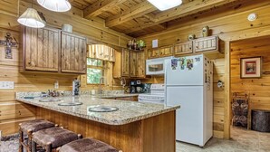 L’intérieur d’une cabane en bois comprend une cuisine équipée d’un plan de travail en granit, d’un réfrigérateur et de meubles de rangement en bois.
