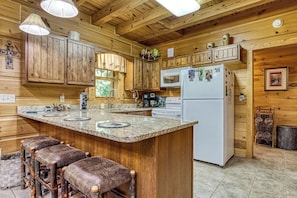 A wooden cabin interior with a kitchen featuring a granite countertop, a refrigerator, and wooden cabinets.