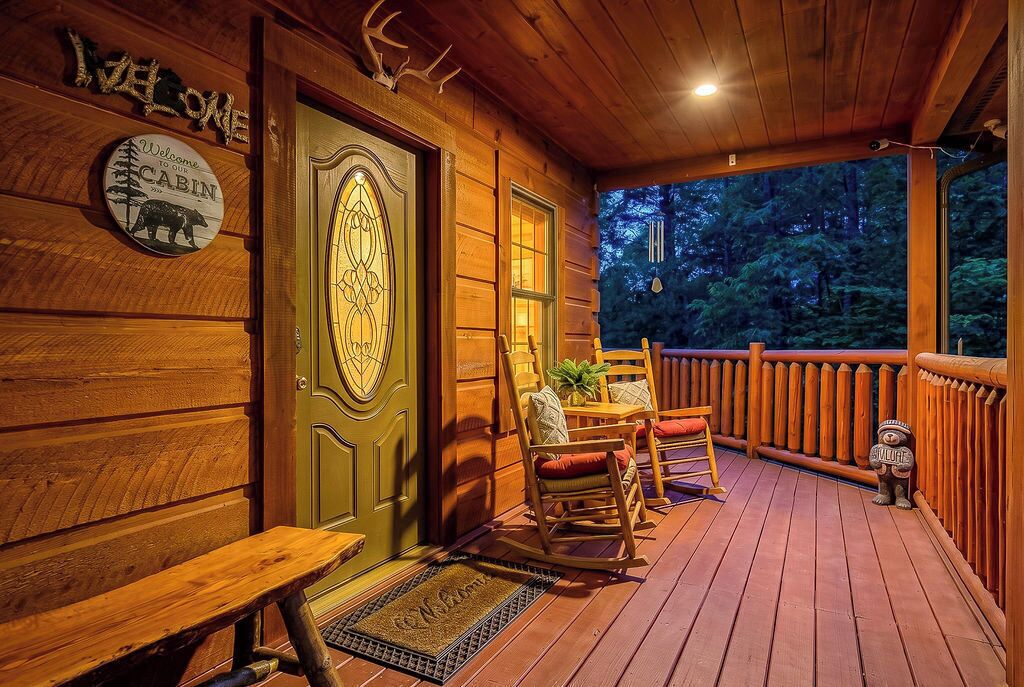 Een cabinentree met een houten deur, een bord met een welkom, een schommelstoel en een bank.