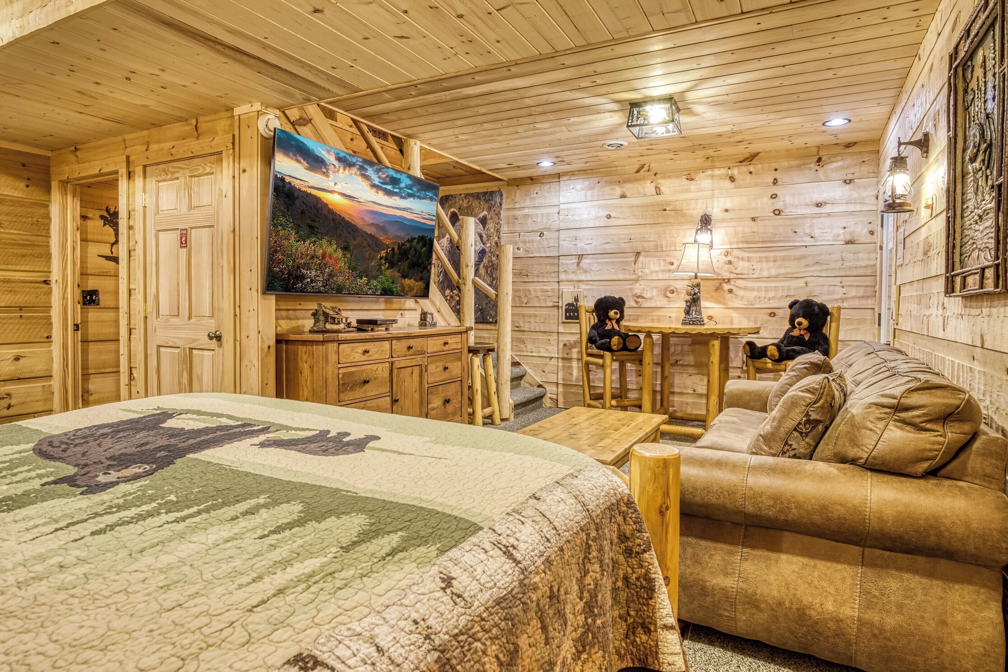 A cozy wooden room with a bed, a sofa, a TV, and a fireplace.