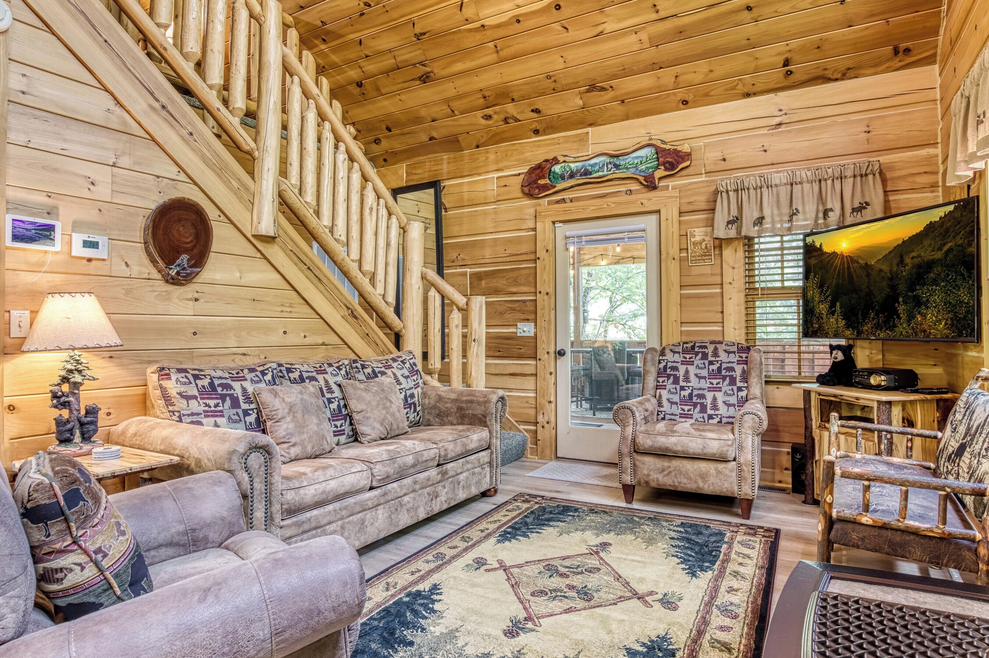 Ein Holzblockhaus-Interieur mit einer Couch, Sesseln, einem Fernseher und einem Kamin.
