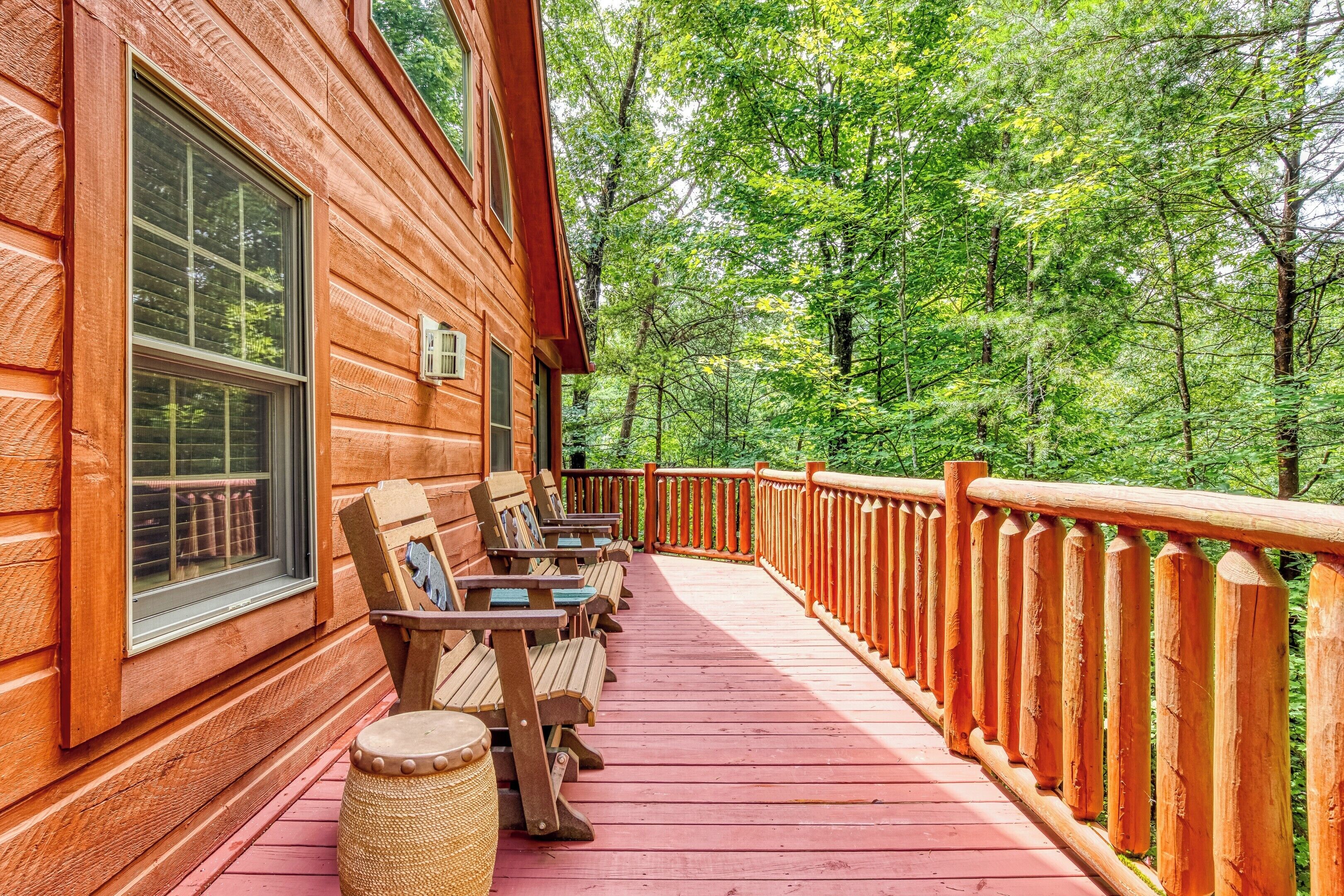 A wooden cabin with a porch, wooden benches, and a railing overlooking a forest.