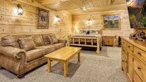 L’intérieur d’une cabane en rondins, avec un canapé, un lit, une table en bois et une commode.