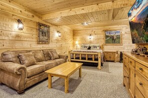 A log cabin interior with a sofa, a bed, a wooden table, and a dresser.