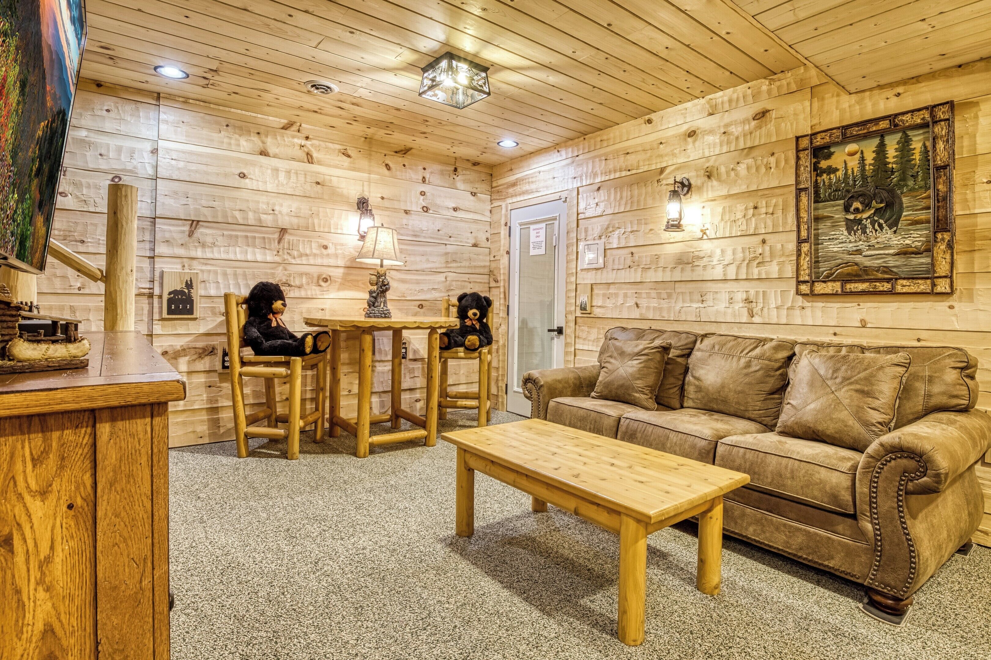 A cozy room with wooden walls, a brown leather sofa, a wooden coffee table, and two chairs with black teddy bears.