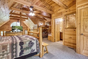 A cozy wooden cabin bedroom with a bunk bed, a desk, and a window overlooking a forest.