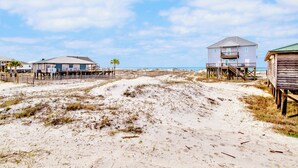 A beach with a wooden structure, a building with a balcony, and a sandy path. - Gulf Front - 5BR - 2BA - 120 Steps to Beach! (Dauphin Island)