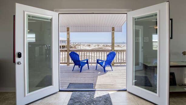 A glass door leading to a deck with two blue chairs and a view of the beach. - Gulf Front - 5BR - 2BA - 120 Steps to Beach! (Dauphin Island)