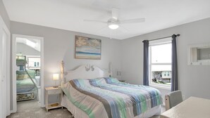 A bedroom with a bed, a nightstand, a desk, a ceiling fan, a window with curtains, and a painting on the wall. - Gulf Front - 5BR - 2BA - 120 Steps to Beach! (Dauphin Island)