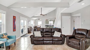 A spacious living room with a brown leather sofa, a blue armchair, and a dining area with a white table. - Gulf Front - 5BR - 2BA - 120 Steps to Beach! (Dauphin Island)
