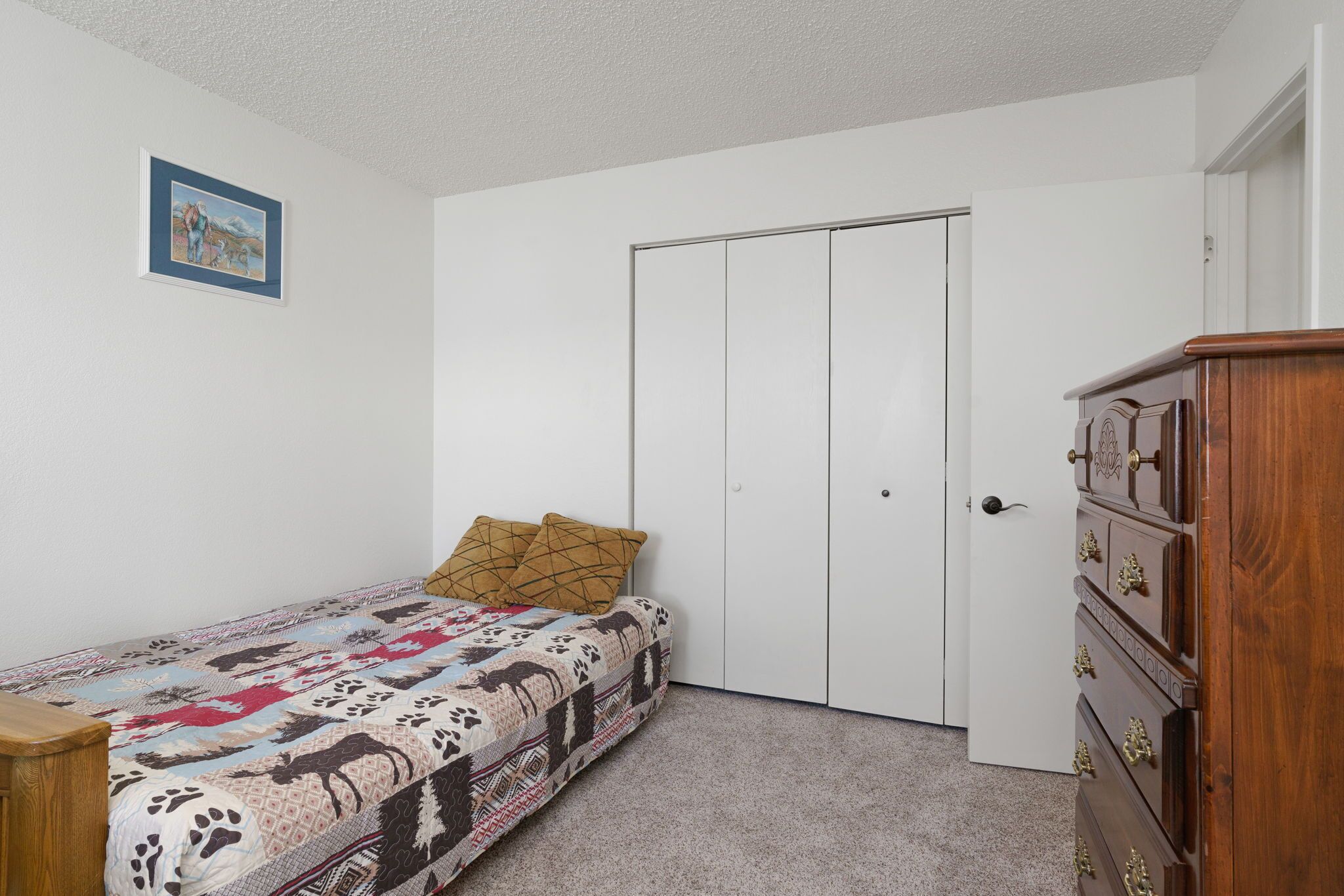 A bedroom with a bed, a dresser, a wardrobe, and a framed picture on the wall.