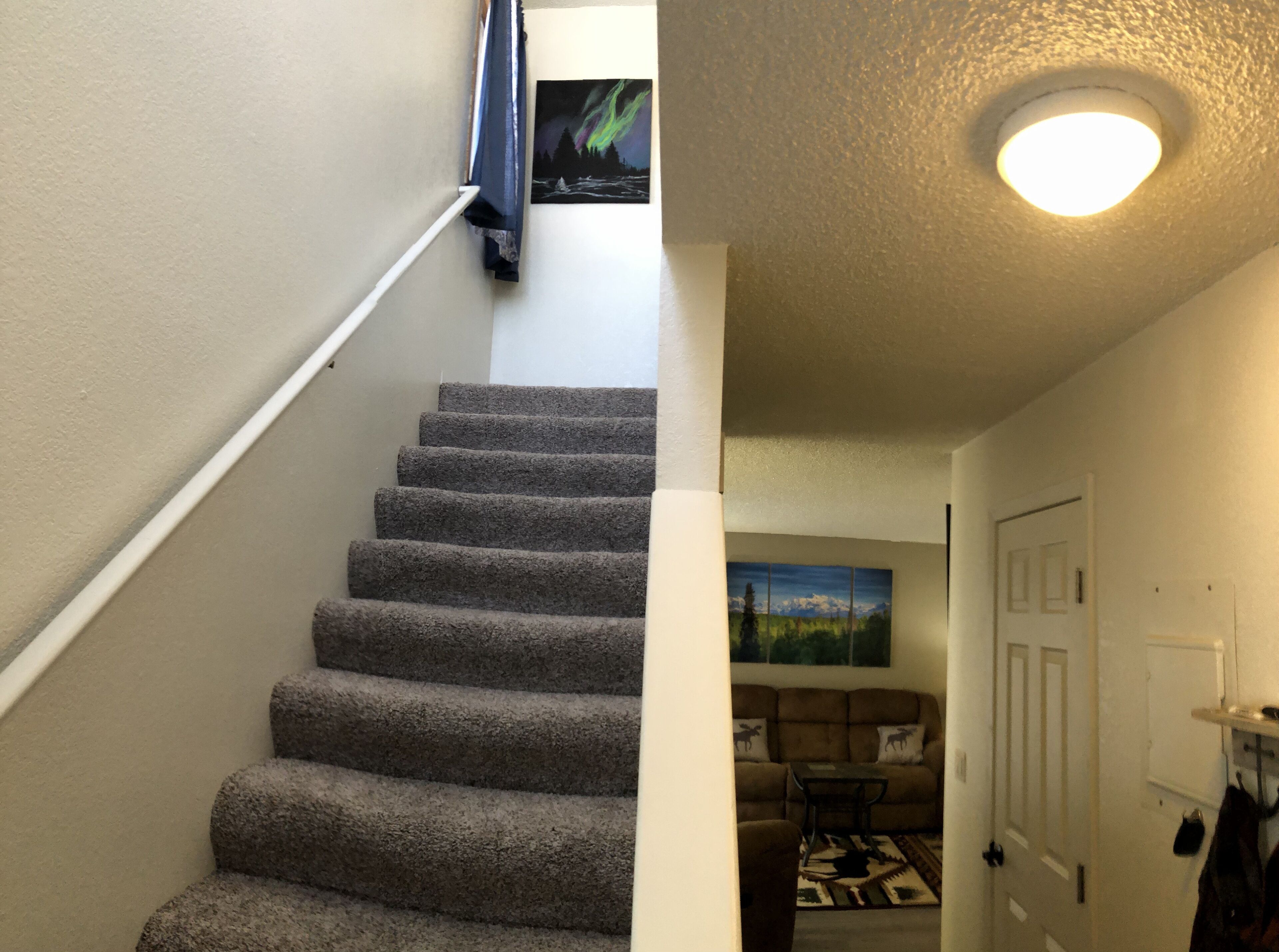 A carpeted staircase leading to a living area with a couch and a painting of a landscape.
