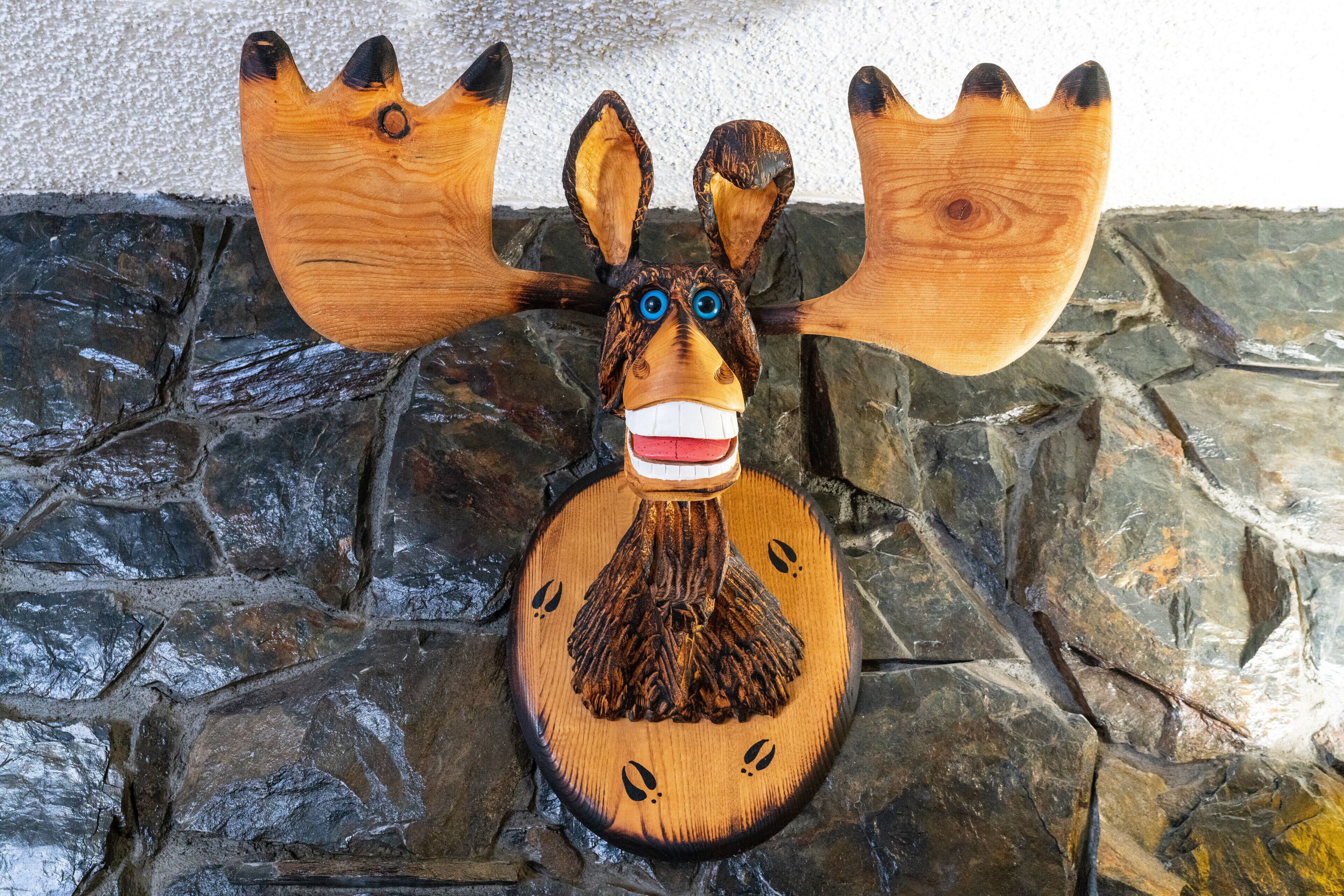 A wooden carving of a moose with antlers, set against a stone wall.