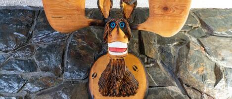 A wooden carving of a moose with antlers, set against a stone wall.