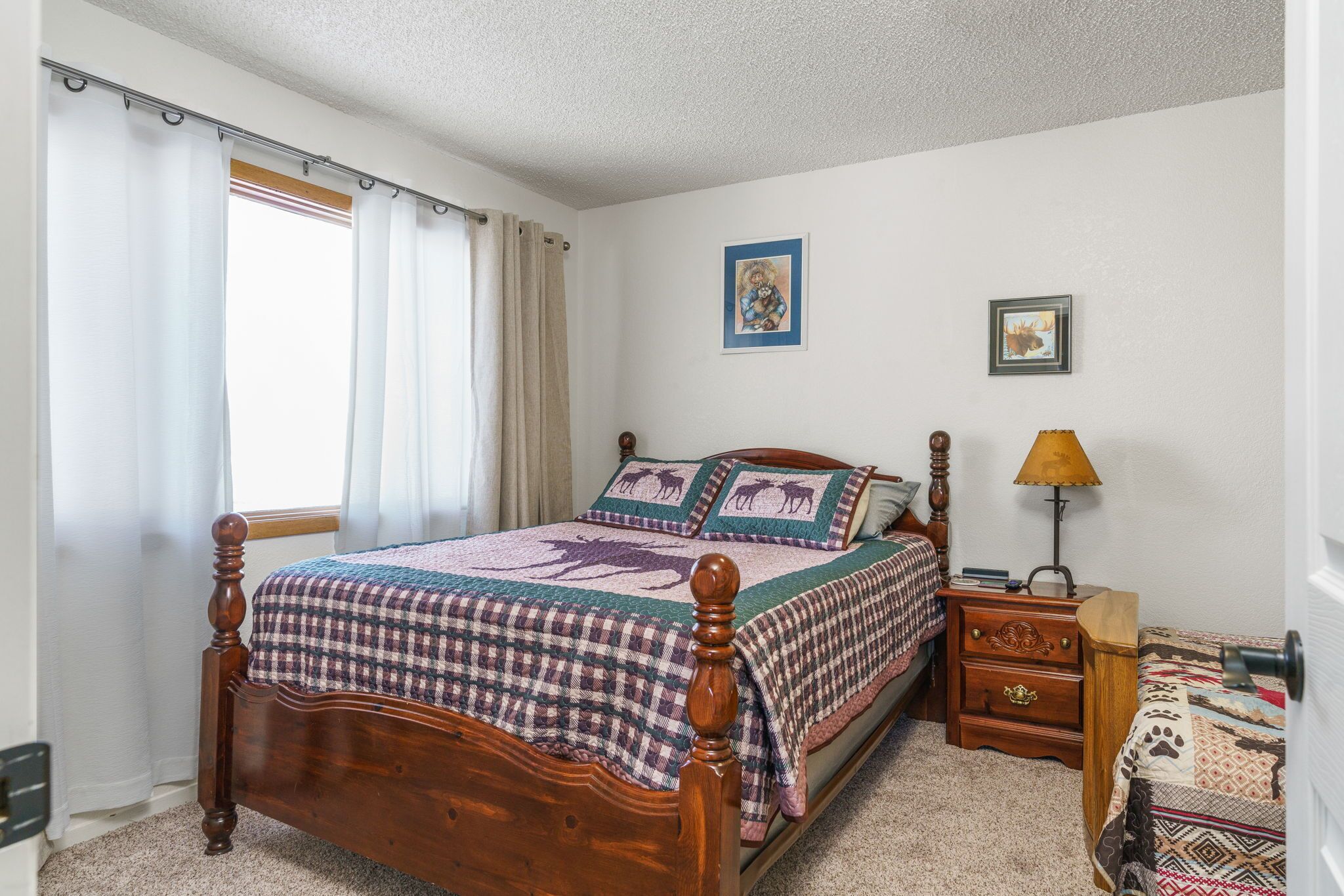 A bedroom with a wooden bed, a nightstand, a lamp, and a window with curtains.