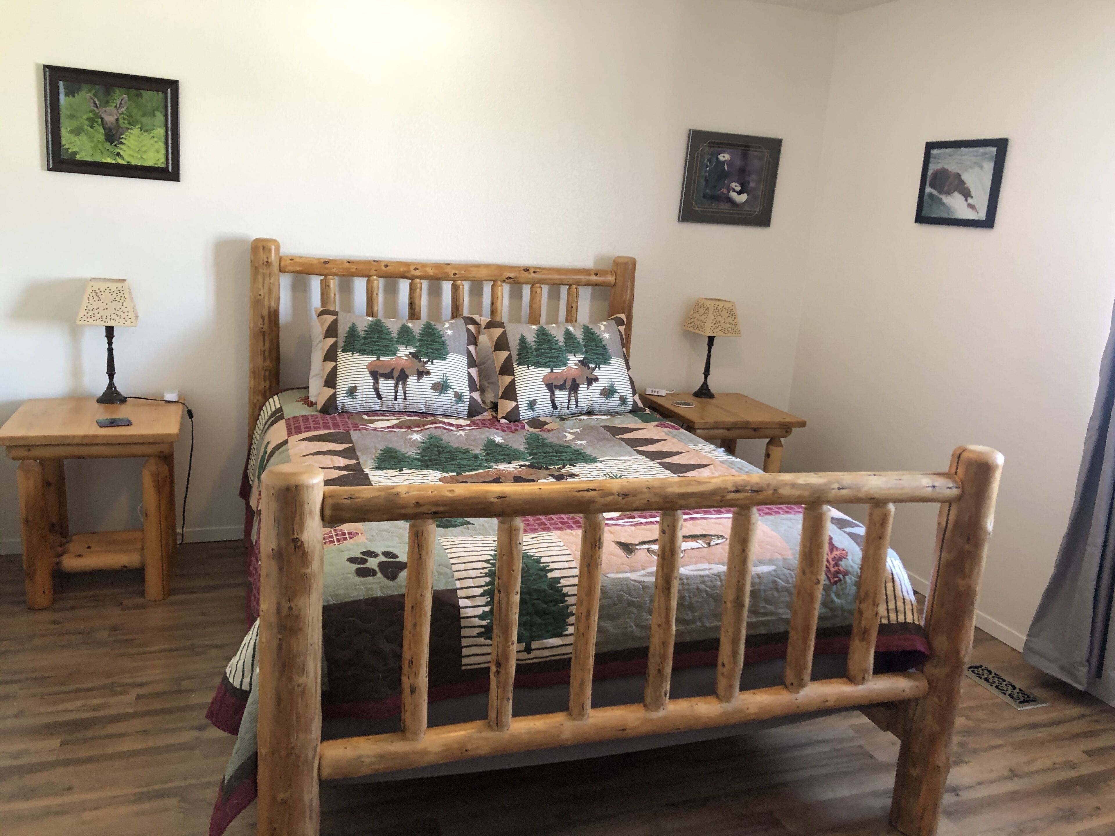 Un lit en bois, agrémenté d’une couvre-lit et de coussins assortis sur le thème de la forêt, et flanqué de deux tables de chevet avec des lampes.