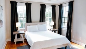 A bedroom with a large bed, two bedside tables with lamps, a wooden nightstand, and a window with curtains. - Chic 2BR Stay | Cozy Living & High-Speed WiFi (Montgomery)