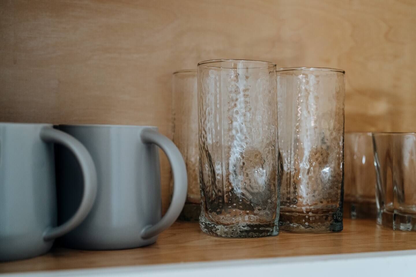 Une étagère contenant divers objets en verre, notamment une tasse grise et plusieurs verres transparents.