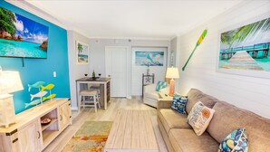 A living room with a wooden coffee table, a beige sofa with colorful cushions, a TV mounted on the wall, and a painting of a beach scene. - BEACHFRONT DIRECT OCEANFRONT PENTHOUSE ONTHE GOLDEN MILE MYRTLE BEACH GRANSTRAND (Myrtle Beach)
