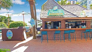 A beachside restaurant with a sign reading "Marco Polo Poolside Grill," outdoor seating with blue chairs, and a wooden kiosk with a menu board. - BEACHFRONT DIRECT OCEANFRONT PENTHOUSE ONTHE GOLDEN MILE MYRTLE BEACH GRANSTRAND (Myrtle Beach)