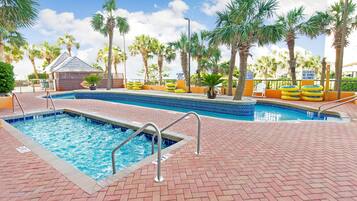 A swimming pool with a brick deck, surrounded by palm trees and a small building.