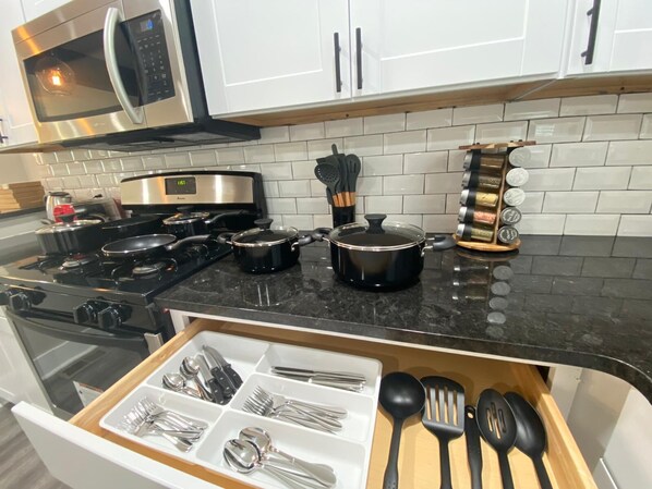A kitchen with a stove, microwave, and various utensils.