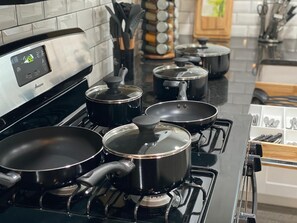 A kitchen with four black pots on a stove, a digital clock, and a knife block.
