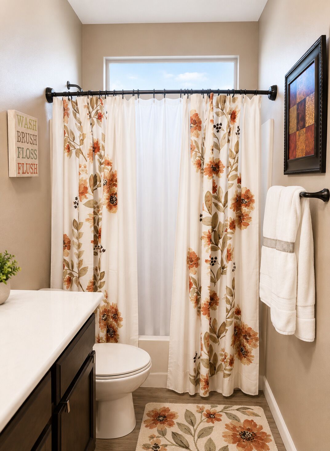 Un baño con inodoro, lavamanos, cortina de ducha con motivos florales, toallero y un cuadro en la pared.