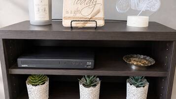 A dark wooden shelf with a Sanyo Blu-ray player, decorative items, and three white ceramic planters with succulents.