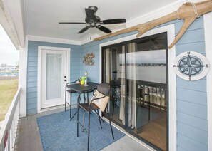 A covered porch with a ceiling fan, a table with chairs, a compass wall decoration, and a view of the outdoors.