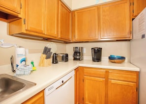 A kitchen with wooden cabinets, a stainless steel sink, a toaster, a coffee maker, and a dish rack.