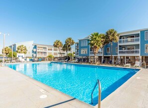 A swimming pool with lounge chairs and palm trees, surrounded by multi-story buildings with balconies.