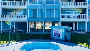 A two-story building with a pool area, including a hot tub and a sign with pool rules.