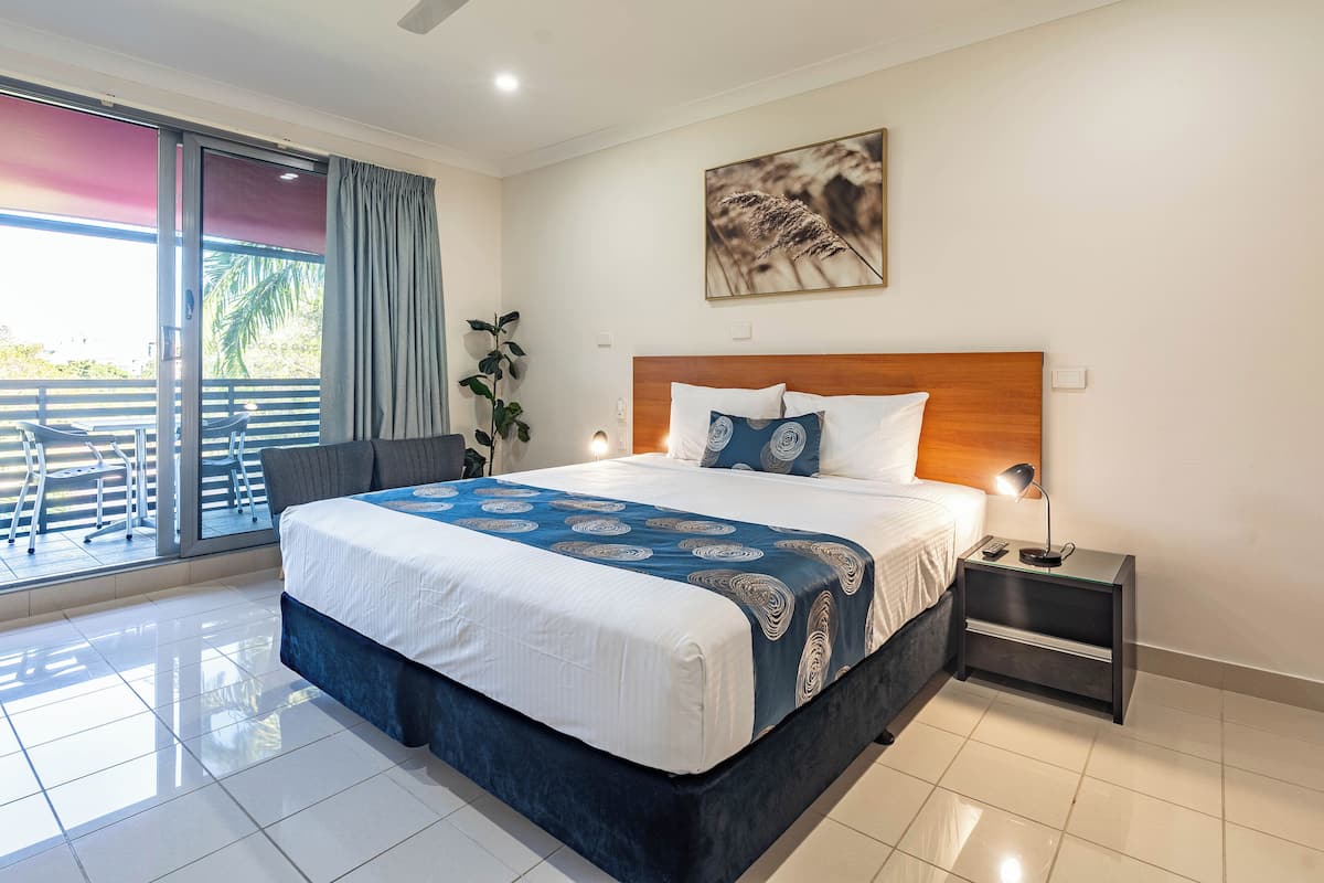 Habitación de hotel moderna con una cama grande, una mesita de noche, un escritorio y un balcón con sillas.