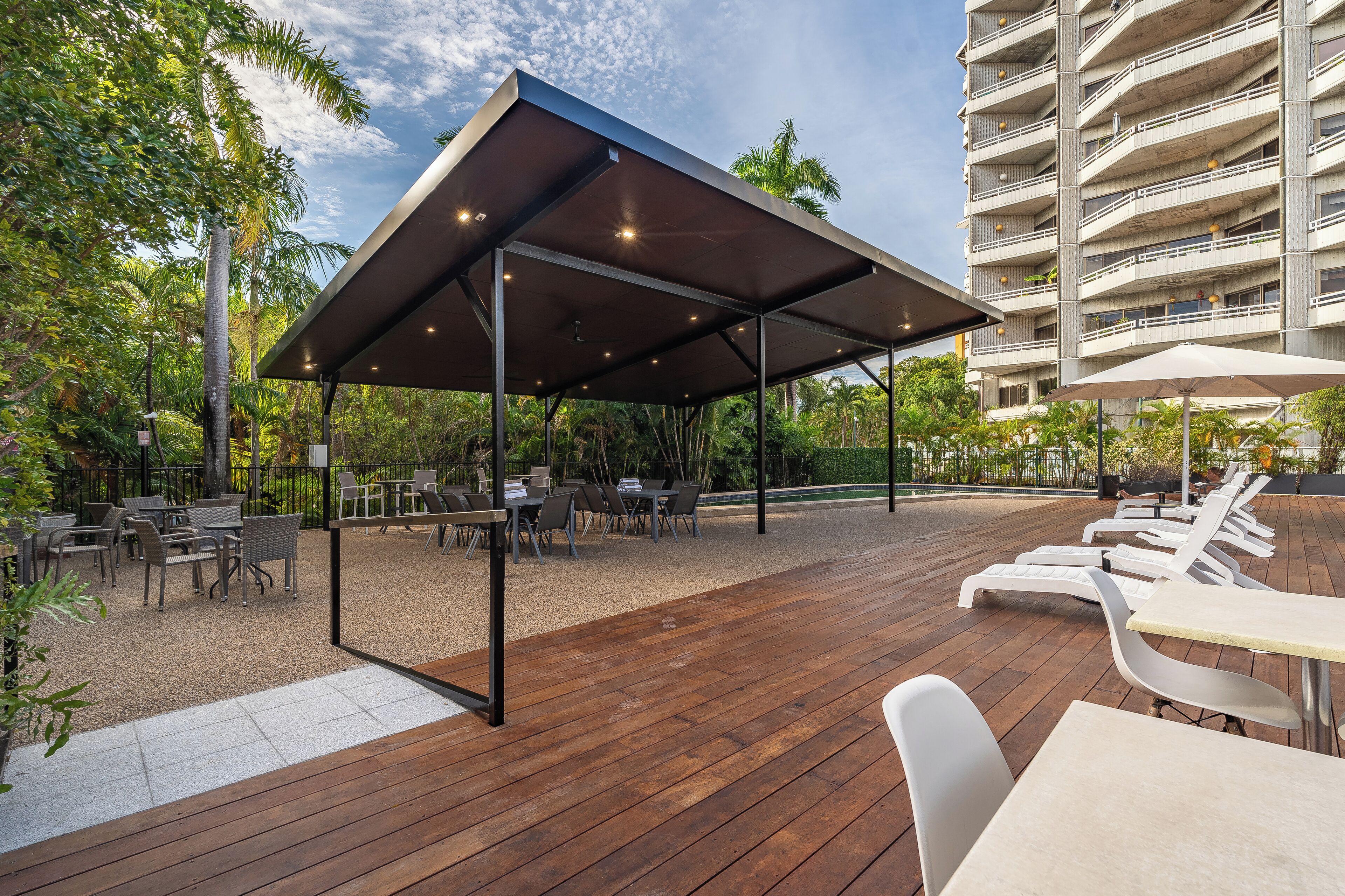 Une terrasse extérieure avec un revêtement de sol en bois, des tables, des chaises et un espace salon abrité.