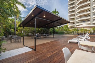 Un patio al aire libre con piso de madera, mesas, sillas y un área de estar cubierta.