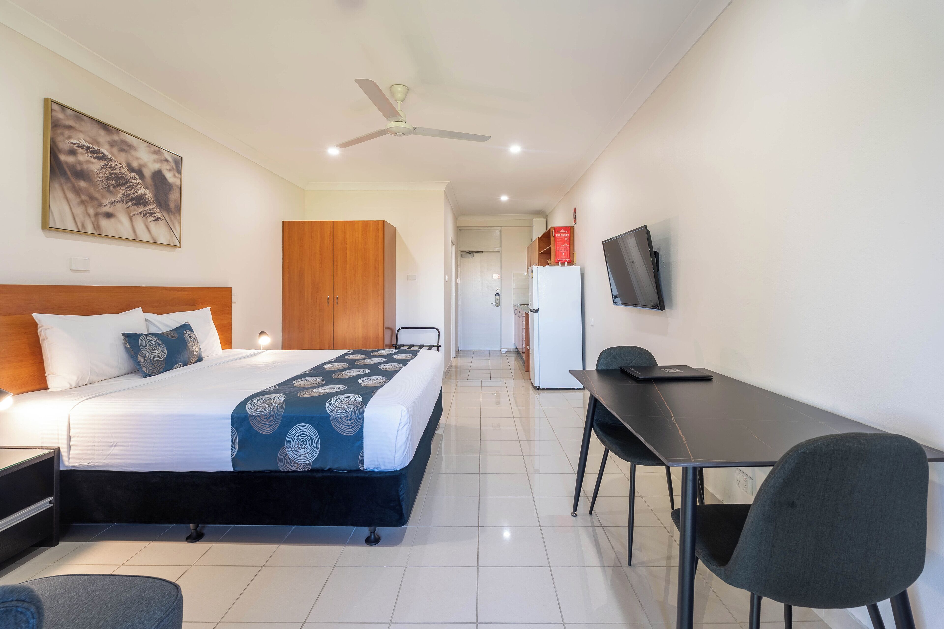 A hotel room with a bed, a desk, a chair, a TV, and a ceiling fan.