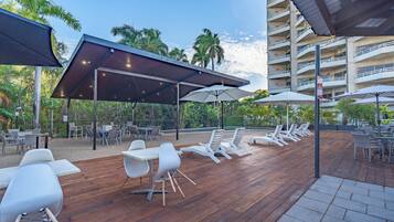 An outdoor patio with wooden flooring, white chairs, and umbrellas.