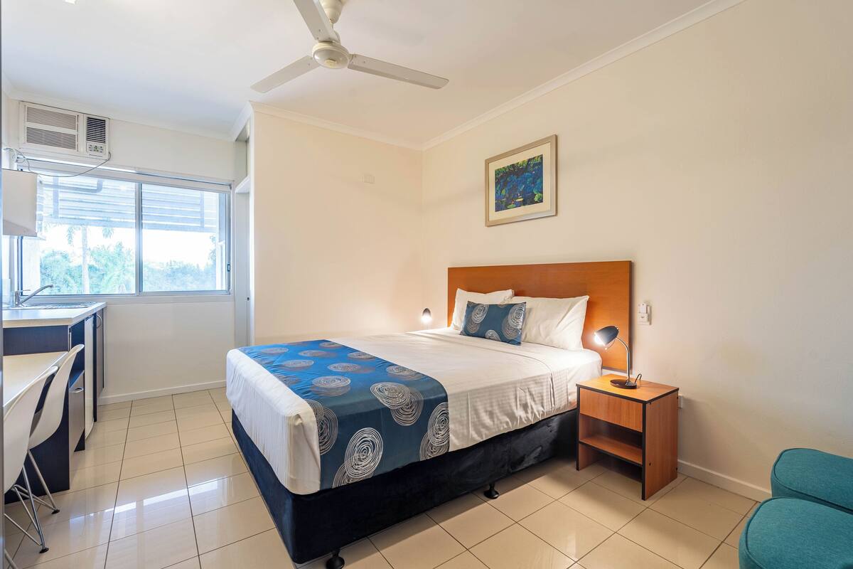 Habitación de hotel con cama, mesita de noche, escritorio, silla y ventilador de techo.