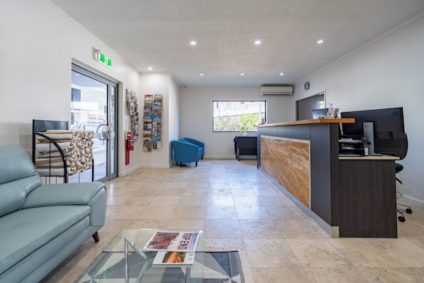 A modern reception area with a reception desk, a blue sofa, a glass coffee table, and a large window providing natural light. - Vitina Studios by Argus (Darwin)