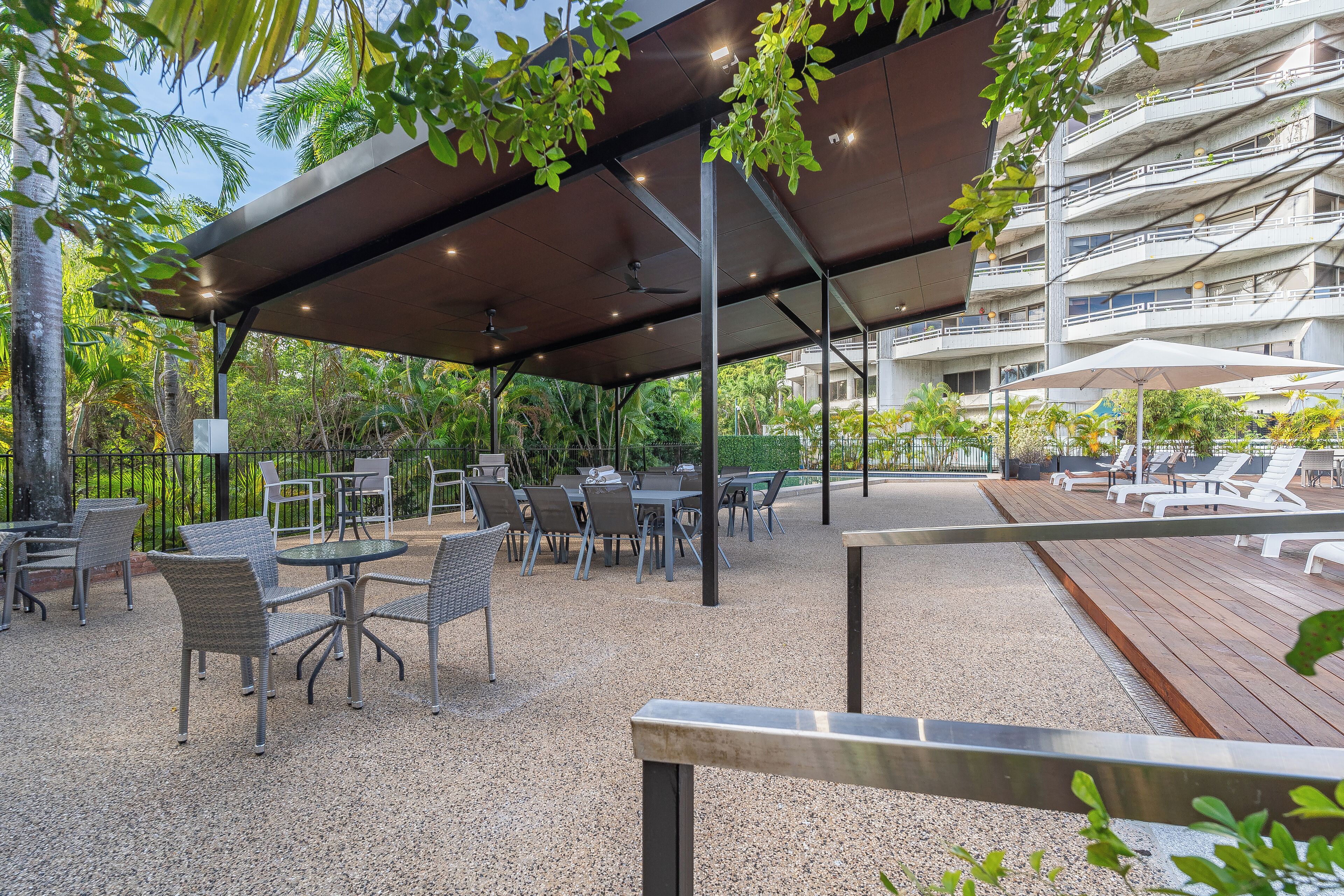 An outdoor patio area with tables and chairs, a covered seating area, and a view of a multi-story building in the background.