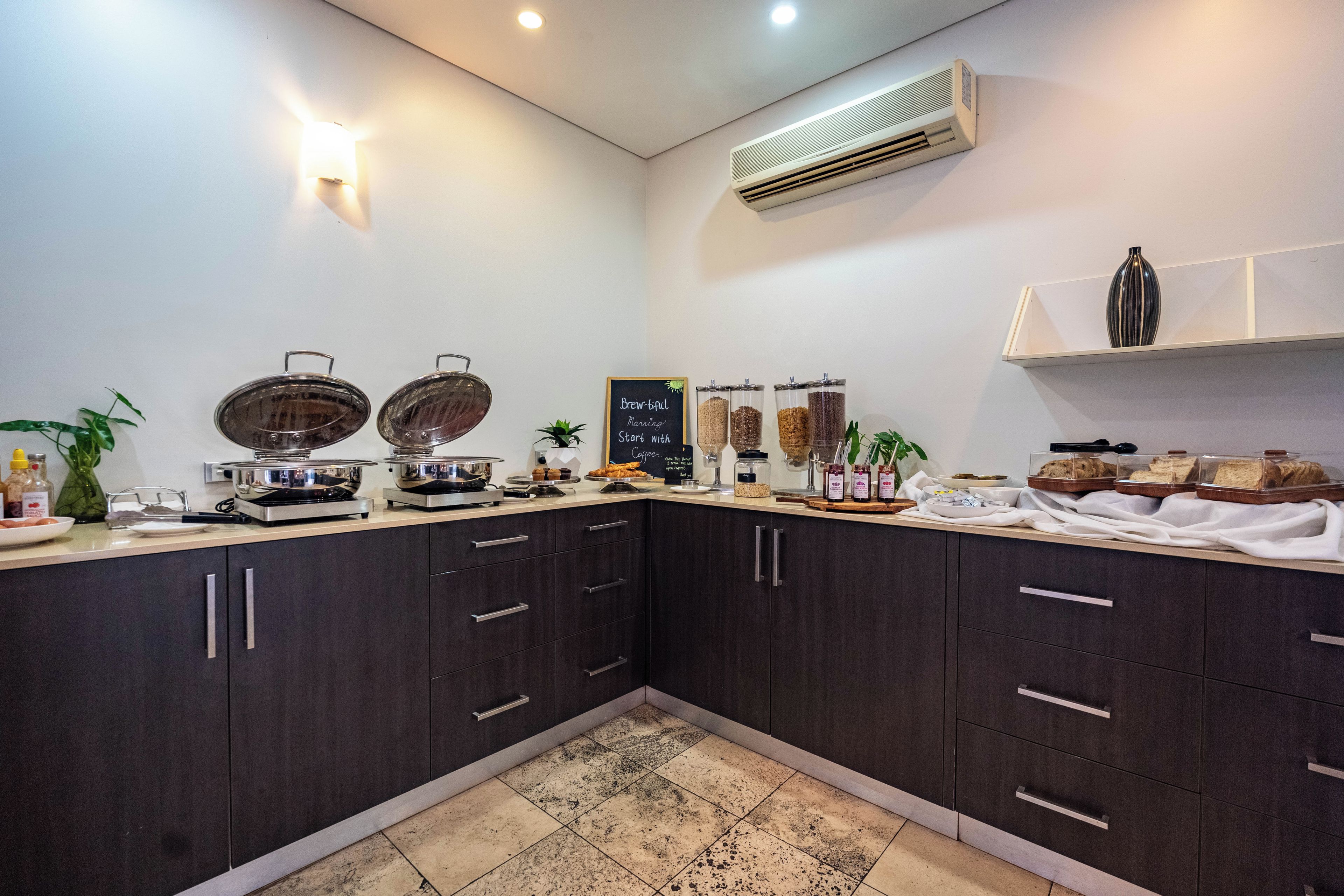 Una cocina con gabinetes oscuros, una encimera con diversos alimentos y un equipo de aire acondicionado en la pared.