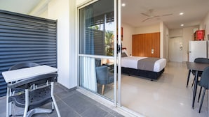 Una moderna camera d'albergo con una porta scorrevole in vetro che dà su un balcone, un letto con testiera in legno, un tavolino e una sedia.