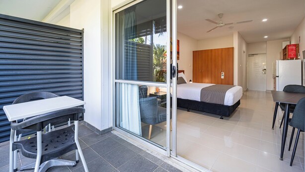 Una habitación de hotel moderna con un puertas corredera de vidrio que da a un balcón, una cama con cabecera de madera, una mesita y una silla.